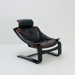 May include: A brown leather armchair with a curved wooden frame and a headrest. The chair has a unique, modern design and is in good condition.