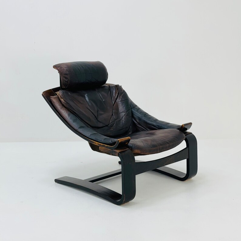 May include: A brown leather armchair with a curved wooden frame and a headrest. The chair has a unique, modern design and is in good condition.