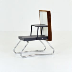 May include: A multi-level chair featuring a tubular chrome metal frame, a black seat, and a smaller black elevated platform. The backrest is a tall, rectangular panel with a white front surface and a brown velvet-textured outer edge.