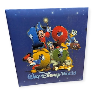Może przedstawiać: Kwadratowa niebieska okładka pamiątkowej książki z napisem 1999 i Walt Disney World. Grafika przedstawia Myszkę Miki jako czarodzieja, Myszkę Minnie, Goofy'ego, Kaczora Donalda i psa Pluto na ciemnoniebieskim tle z akcentami w kształcie gwiazd.