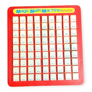 May include: A red multiplication learning tool with white number tiles. The text "Magic Math Machine MULTIPLICATION" is at the top. The tiles are arranged in a grid, displaying multiplication problems from 1x1 to 9x9.