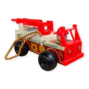 Könnte beinhalten: Vintage Fisher-Price Fire Engine Spielzeug. Das Spielzeug-Feuerwehrauto ist rot, weiß und gelb mit schwarzen Rädern. Das Spielzeug hat eine rote Leiter und eine Schnur. Die Worte "Price Fire Engine" sind auf der Seite aufgedruckt.