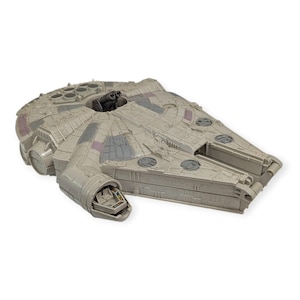 Puede incluir: Un modelo detallado de la nave espacial Millennium Falcon, con una combinación de colores gris claro con detalles en gris oscuro y morado. El modelo tiene intrincados paneles y detalles de diseño, con una torreta de cañón central y cabina.