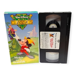 Puede incluir: Un conjunto de cinta VHS y caja vintage de "Walt Disney Mini Classics: Mickey y las Habichuelas Mágicas". La caja presenta ilustraciones coloridas de Mickey Mouse y otros personajes. La cinta VHS es negra con una etiqueta blanca.