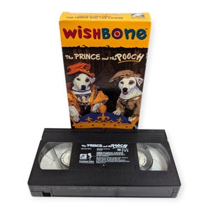 May include: A VHS tape and box set for "Wishbone: The Prince and the Pooch." The box is yellow and features two dogs dressed in royal attire. The VHS tape is black with white text.