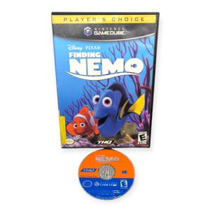 Può includere: Una custodia e un disco per videogiochi Nintendo GameCube del film Disney Pixar "Alla ricerca di Nemo". La custodia presenta Nemo e Dory in una scena subacquea. Il disco è arancione e blu con il titolo del film.