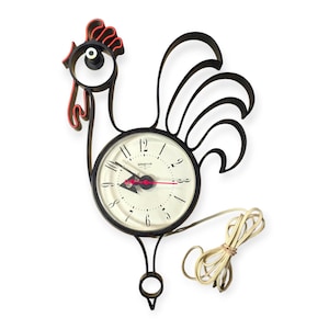 May include: A vintage wall clock shaped like a rooster. The clock has a black metal frame with a red comb and wattle. The clock face is white with black numbers and hands, and the second hand is red. The clock is labeled "Spartus".