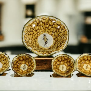 May include: Set of five small glass bowls with a peanut design. The bowls are decorated with a cartoon peanut character wearing a top hat and holding a cane. The bowls are arranged in a row on a wooden surface.