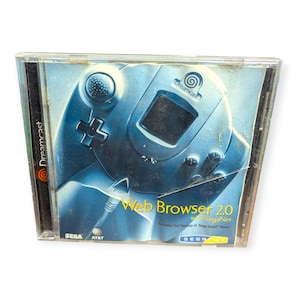 Puede incluir: Un disco de juego Dreamcast Web Browser 2.0 en una caja de plástico transparente. La portada presenta una imagen en tonos azules de un mando de Dreamcast. El texto "Web Browser 2.0 with SegaNet" es visible. También están los logotipos de Sega y AT&T.