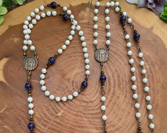 Peut inclure: Deux chapelets en perles blanches avec des perles violettes et brunes, chacun avec un crucifix en bronze et un médaillon en bronze du visage de Jésus.