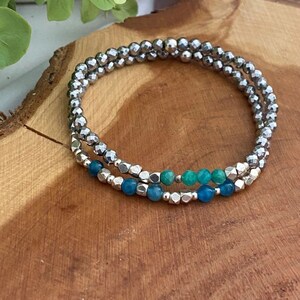 May include: A silver beaded bracelet with a row of blue and green gemstone beads.
