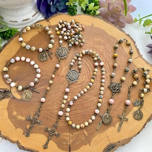 May include: Four different rosaries made with pink and yellow agate beads and antique bronze accents. Each rosary features a cross and a pendant with a religious image.