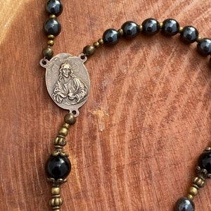 Peut inclure: Un chapelet noir et or avec un pendentif en m&eacute;tal repr&eacute;sentant une image en relief de J&eacute;sus-Christ. Les perles du chapelet sont en onyx noir et en h&eacute;matite.