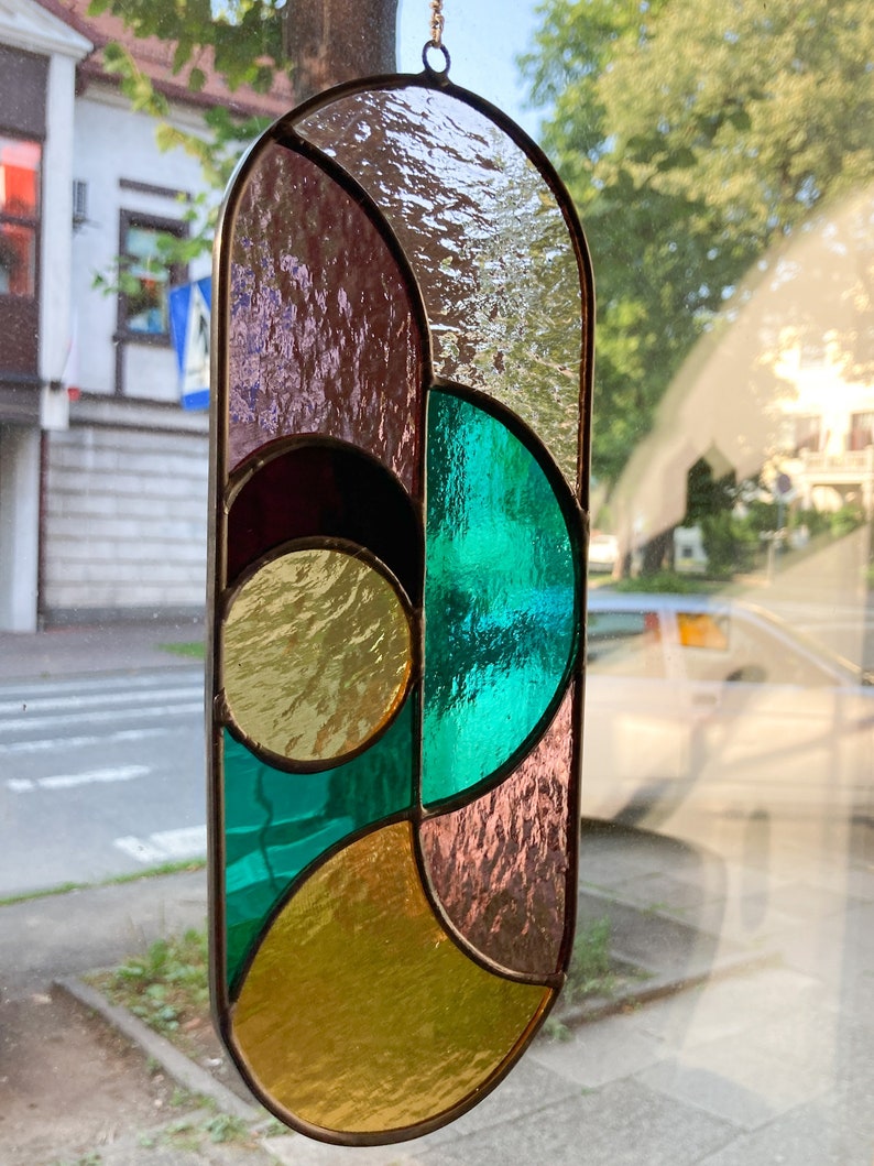 May include: A stained glass window hanging features a geometric design with teal, gold, and purple glass pieces.
