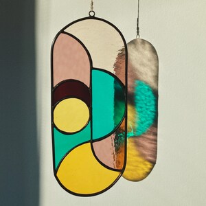 May include: A stained glass window hanging with geometric shapes in shades of pink, yellow, teal, and brown.