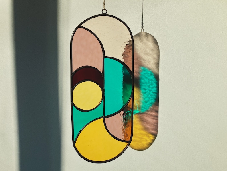 May include: A stained glass window hanging with geometric shapes in shades of pink, yellow, teal, and brown.