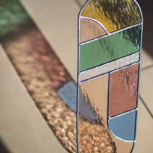 May include: A stained glass panel with geometric shapes in shades of brown, green, blue, and yellow. The panel is oval-shaped and has a silver frame.