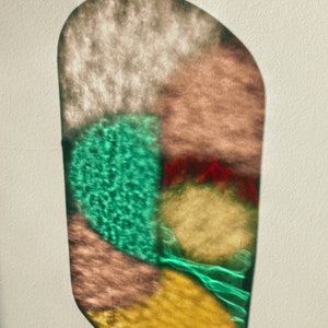 May include: A stained glass suncatcher with a variety of colors, including green, red, yellow, and brown. The suncatcher is shaped like an oval and has a chain attached to the top.