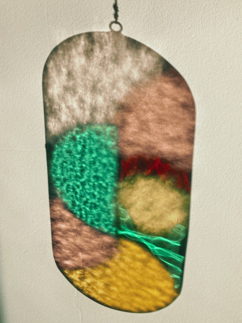 May include: A stained glass suncatcher with a variety of colors, including green, red, yellow, and brown. The suncatcher is shaped like an oval and has a chain attached to the top.