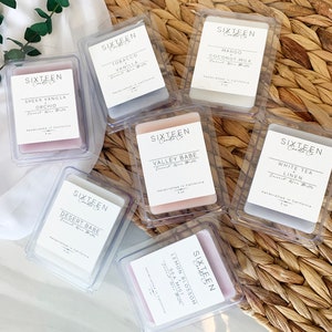 May include: Assortment of small, clear, square containers with labels for scented candles. The labels feature the text "Sixteen Candle Co." and various scents, including "Sheer Vanilla Orchid", "Tobacco Vanilla", "Mango Coconut Milk", "Valley Babe", "White Tea Linen", "Desert Babe", and "Lemon Blossom Sea Mist".