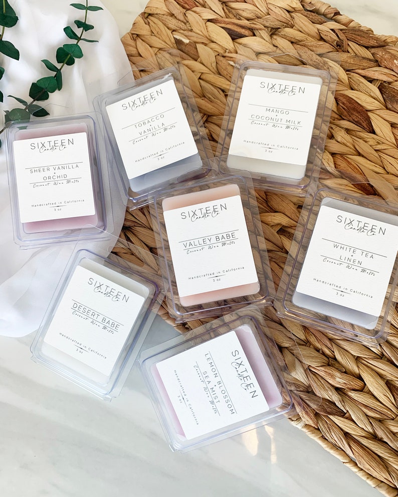 May include: Assortment of small, clear, square containers with labels for scented candles. The labels feature the text "Sixteen Candle Co." and various scents, including "Sheer Vanilla Orchid", "Tobacco Vanilla", "Mango Coconut Milk", "Valley Babe", "White Tea Linen", "Desert Babe", and "Lemon Blossom Sea Mist".