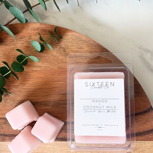 May include: Three pink wax melts in a clear plastic container. The label reads "Sixteen Candle Co. Mango + Coconut Milk Coconut Wax Melts Handcrafted in California 3 oz."