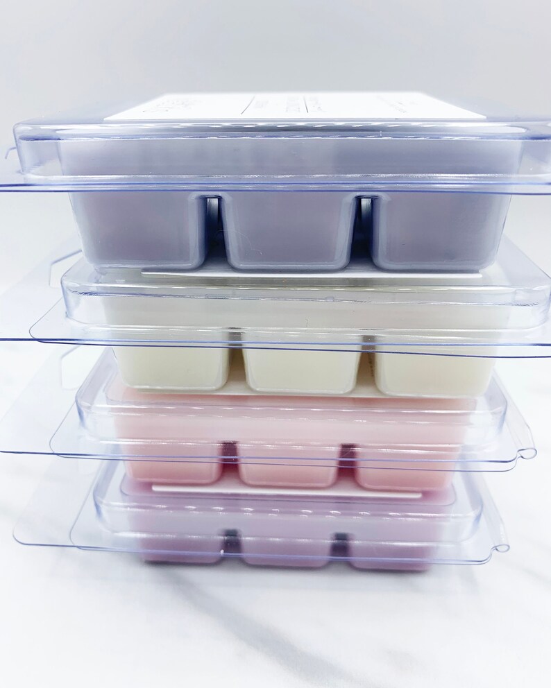May include: A stack of four clear plastic containers with six individual wax melts in each. The wax melts are in different colors, including purple, white, and pink.