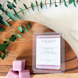 May include: A set of three purple wax melts in a clear plastic container. The label reads "Sixteen Candle Co. Tobacco Vanilla Coconut Wax Melts Handcrafted in California 3 oz."