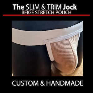 May include: A beige jockstrap with a stretch pouch and a white waistband. The jockstrap is displayed on a black mannequin. Text at the top reads "The SLIM & TRIM Jock BEIGE STRETCH POUCH". The text "CUSTOM & HANDMADE" is at the bottom.