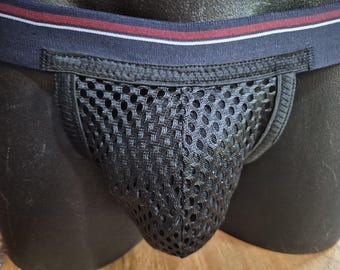 Pode incluir: Um suspensório de malha preta com uma larga faixa elástica em azul-marinho, acentuada com uma faixa vermelha horizontal e um fino debrum branco. A bolsa frontal é feita de um tecido de malha preta respirável com orifícios abertos.