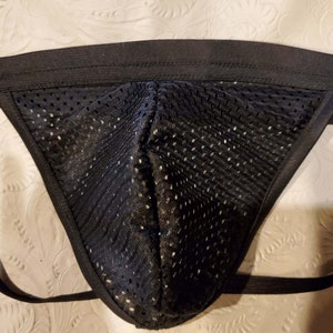 Pode incluir: Jockstrap de malha preta com al&ccedil;as ajust&aacute;veis. As al&ccedil;as s&atilde;o feitas de material el&aacute;stico preto.