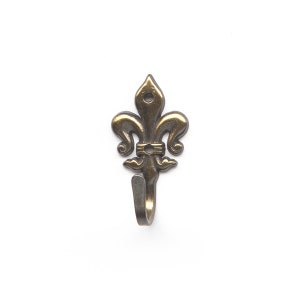 May include: A gold-toned metal hook with a fleur-de-lis design. The hook is attached to a wall.