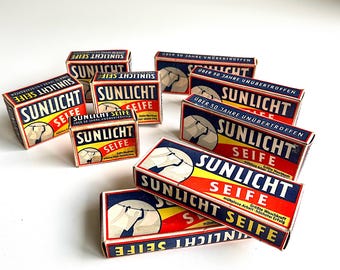 May include: A collection of vintage Sunlight Seife soap boxes. The boxes feature a red, yellow, and blue color scheme with the brand name prominently displayed. The boxes also include the text "Über 50 Jahre unübertroffen."