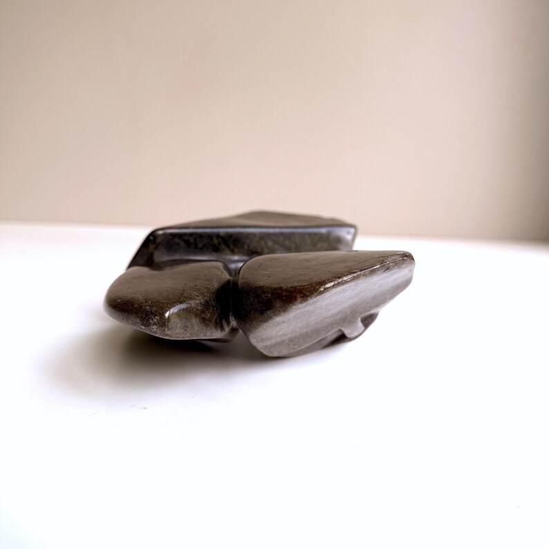 May include: Three polished, dark brown stones with a smooth, reflective surface. The stones are arranged in a cluster, with varying shapes and sizes. The lighting highlights the natural textures and subtle color variations of the stones.