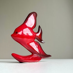 Könnte beinhalten: Eine rote und schwarze Keramikfigur eines Fisches mit einer langen, fließenden Flosse. Der Fisch steht auf einem kleinen, roten Sockel.