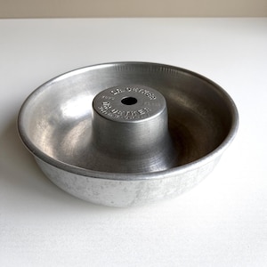 Könnte beinhalten: Eine Vintage-Gugelhupf-Backform aus Aluminium mit einem zentralen Rohr. Die Form hat eine kreisförmige Form mit breitem Boden und erhabener Mitte. Die Worte "DR. OETKER" sind auf dem Mittelrohr eingeprägt. Ein klassisches Backwerkzeug.