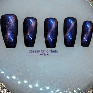 May include: Set of five long, coffin-shaped false nails with a dark blue and purple magnetic polish. The nails have a shimmery, iridescent finish.