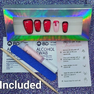Puede incluir: Un juego de u&ntilde;as postizas a presi&oacute;n en una caja hologr&aacute;fica plateada, con un dise&ntilde;o rojo y negro de estilo caricatura. Incluye toallitas con alcohol, una lima de u&ntilde;as, un empujador de cut&iacute;culas de madera e instrucciones. La palabra "Included" est&aacute; en la parte inferior.