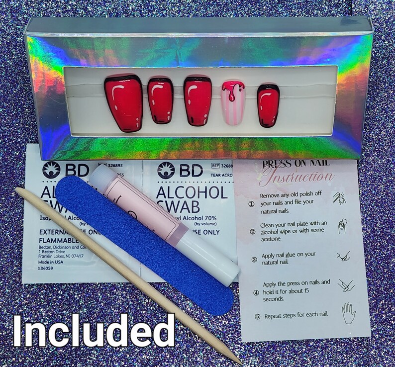 Puede incluir: Un juego de u&ntilde;as postizas a presi&oacute;n en una caja hologr&aacute;fica plateada, con un dise&ntilde;o rojo y negro de estilo caricatura. Incluye toallitas con alcohol, una lima de u&ntilde;as, un empujador de cut&iacute;culas de madera e instrucciones. La palabra "Included" est&aacute; en la parte inferior.