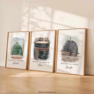 May include: Three framed art prints featuring watercolor illustrations of Islamic landmarks: Masjid Al-Nabawi, Masjid Al-Haram, and Masjid Al-Aqsa. Each print has a gold frame and includes the name of the mosque and its location.