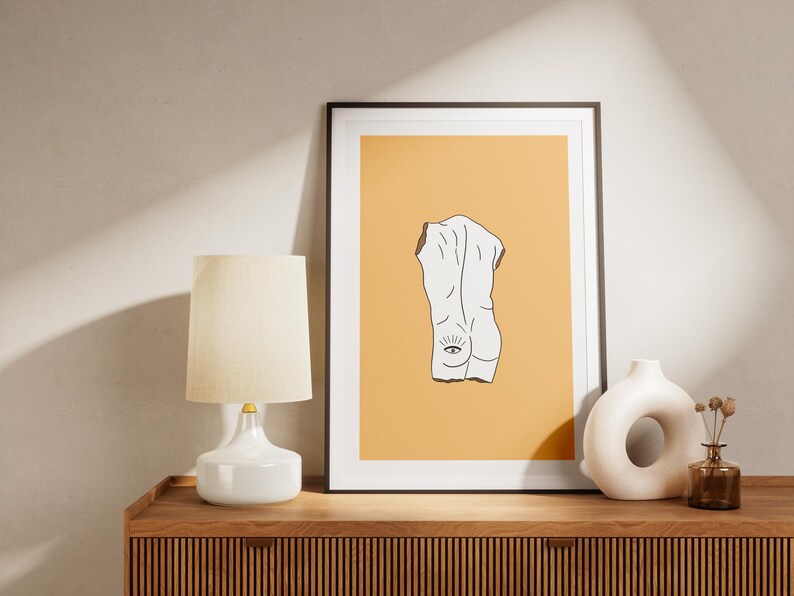 Peut inclure: Une impression encadr&eacute;e avec un dessin au trait minimaliste d'une figure nue avec un &oelig;il au dos. Le fond est de couleur orange clair.