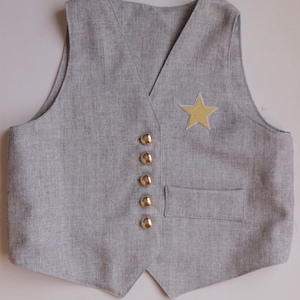 K&ouml;nnte beinhalten: Eine graue Weste mit einem goldenen Stern-Patch und goldenen Kn&ouml;pfen.