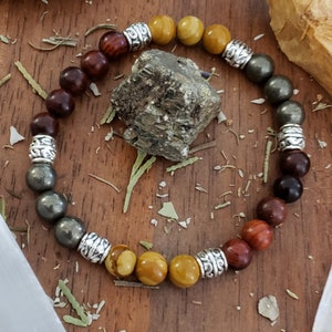 May include: A multi-colored beaded bracelet with silver accents. The bracelet features brown, yellow, and gray beads.