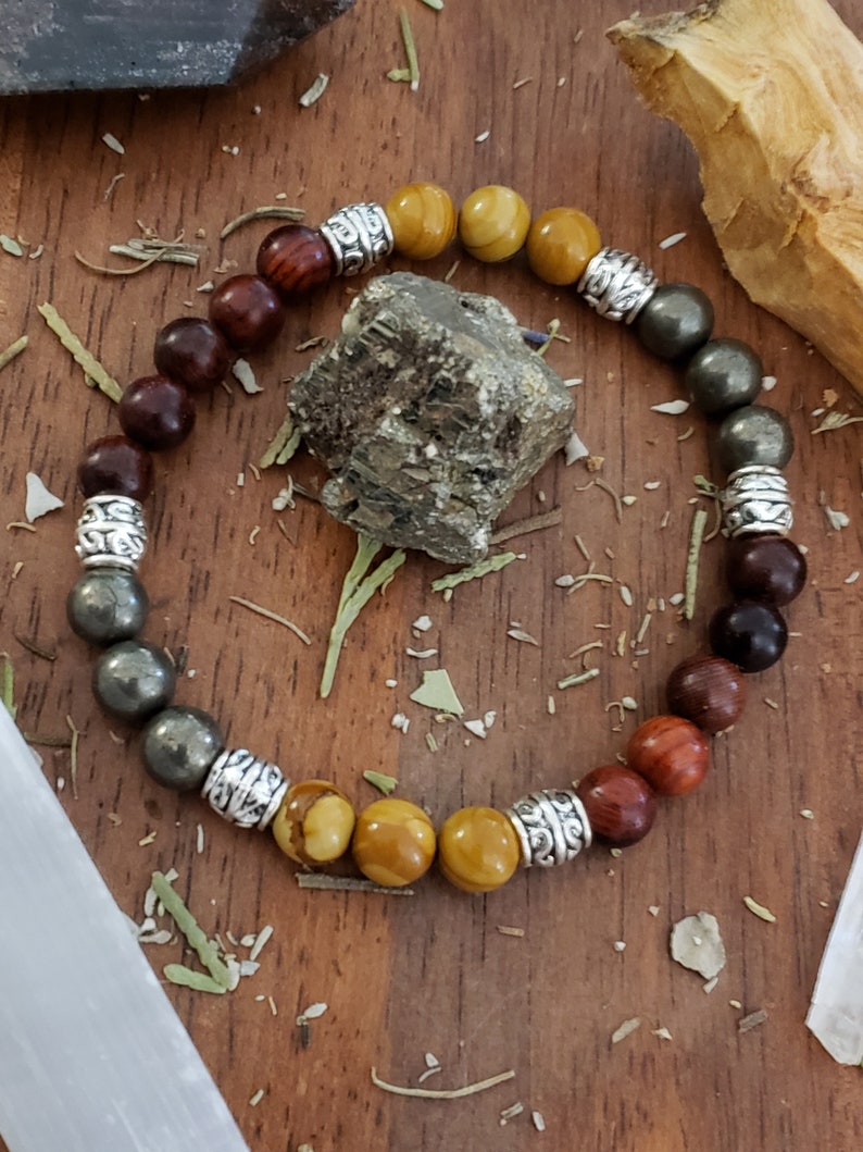 May include: A multi-colored beaded bracelet with silver accents. The bracelet features brown, yellow, and gray beads.