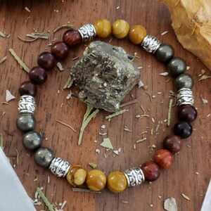 May include: A multi-colored beaded bracelet with silver accents. The bracelet features brown, yellow, and gold beads.