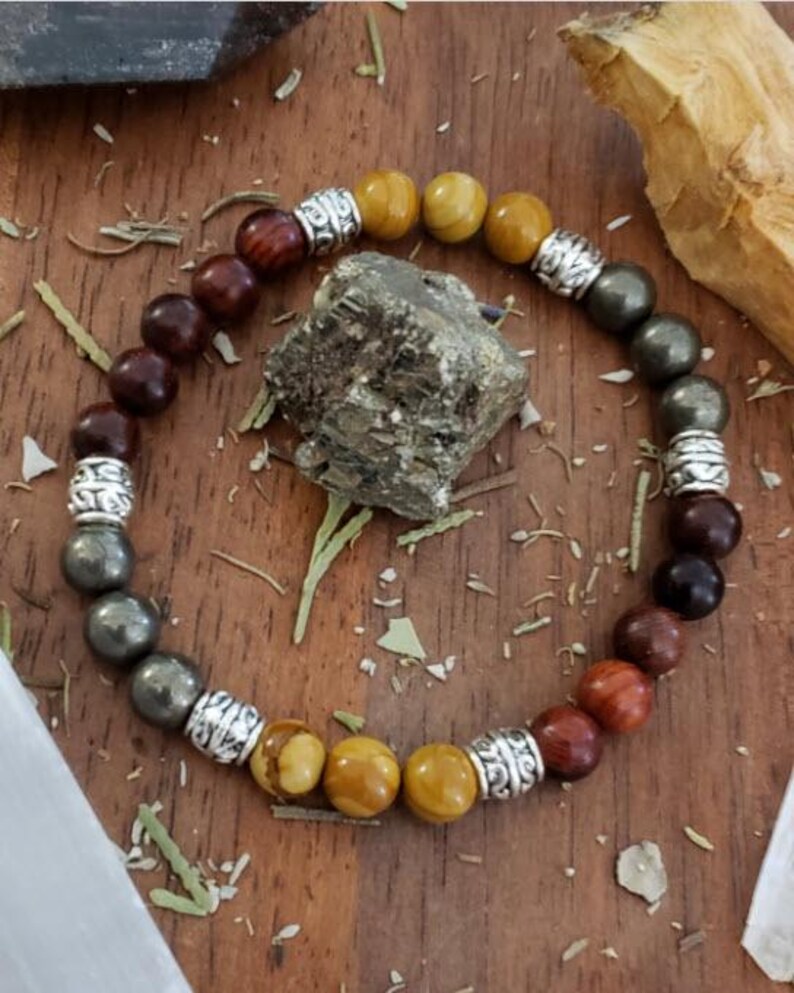 May include: A multi-colored beaded bracelet with silver accents. The bracelet features brown, yellow, and gold beads.