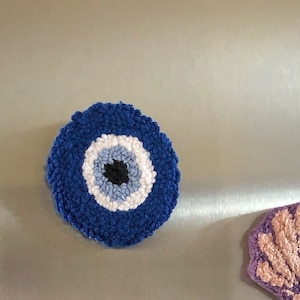 Könnte beinhalten: Ein blauer und weißer Glücksbringer mit einem schwarzen Auge, aus Garn gefertigt und in runder Form.
