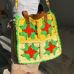 May include: A yellow, green, and orange crocheted tote bag with a brown leather handle and a gold chain strap.