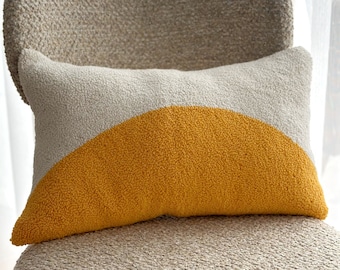 May include: A beige and yellow throw pillow with a half-circle design. The pillow is sitting on a beige chair.