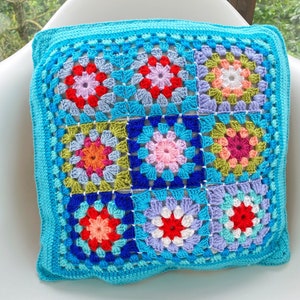 May include: A turquoise blue crocheted cushion with a colourful granny square pattern. The squares are made with various shades of blue, green, red, pink and white yarn.